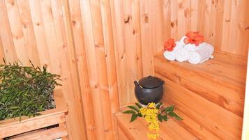 A wooden sauna with a black pot, towels, and a potted plant.