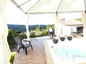 A covered outdoor area with a hot tub, lounge chairs, and a table with glasses.