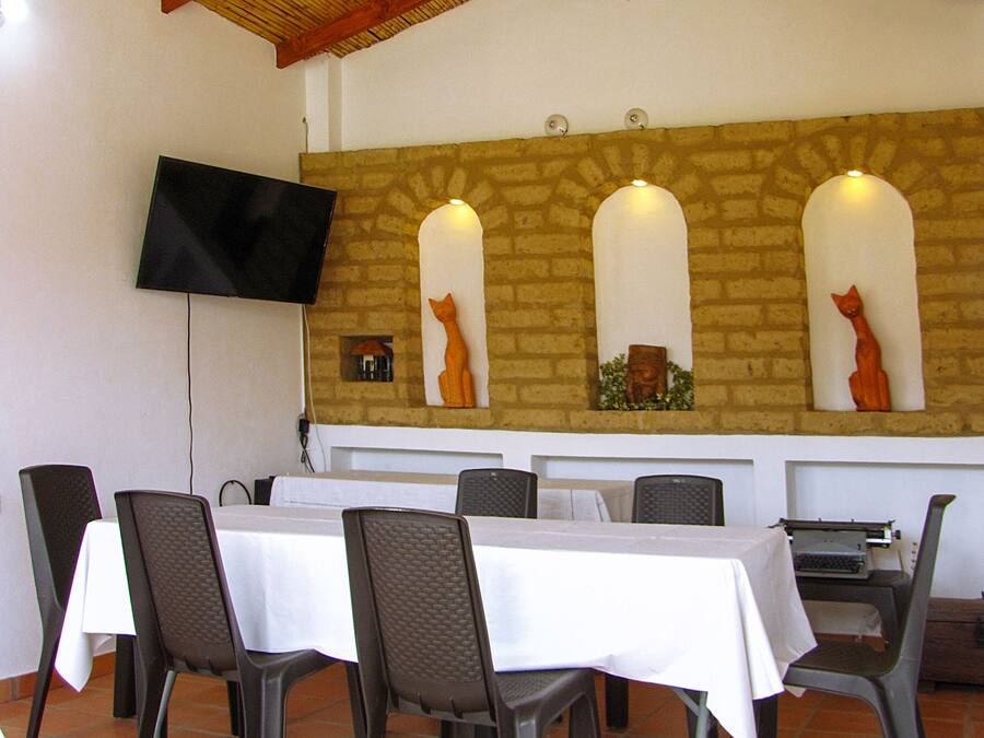 Un comedor con suelo de baldosas, una pared de piedra con nichos de arco y un televisor de pantalla plana montado en la pared.