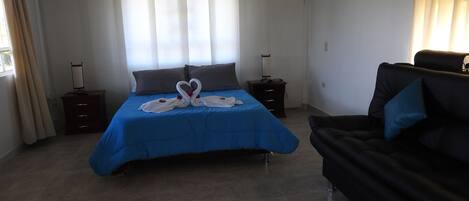 Una habitación de hotel con cama, sofá, mesita de noche y ventana con cortinas.