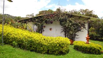 A small building with a white exterior, surrounded by well-maintained green hedges and a variety of flowering plants.