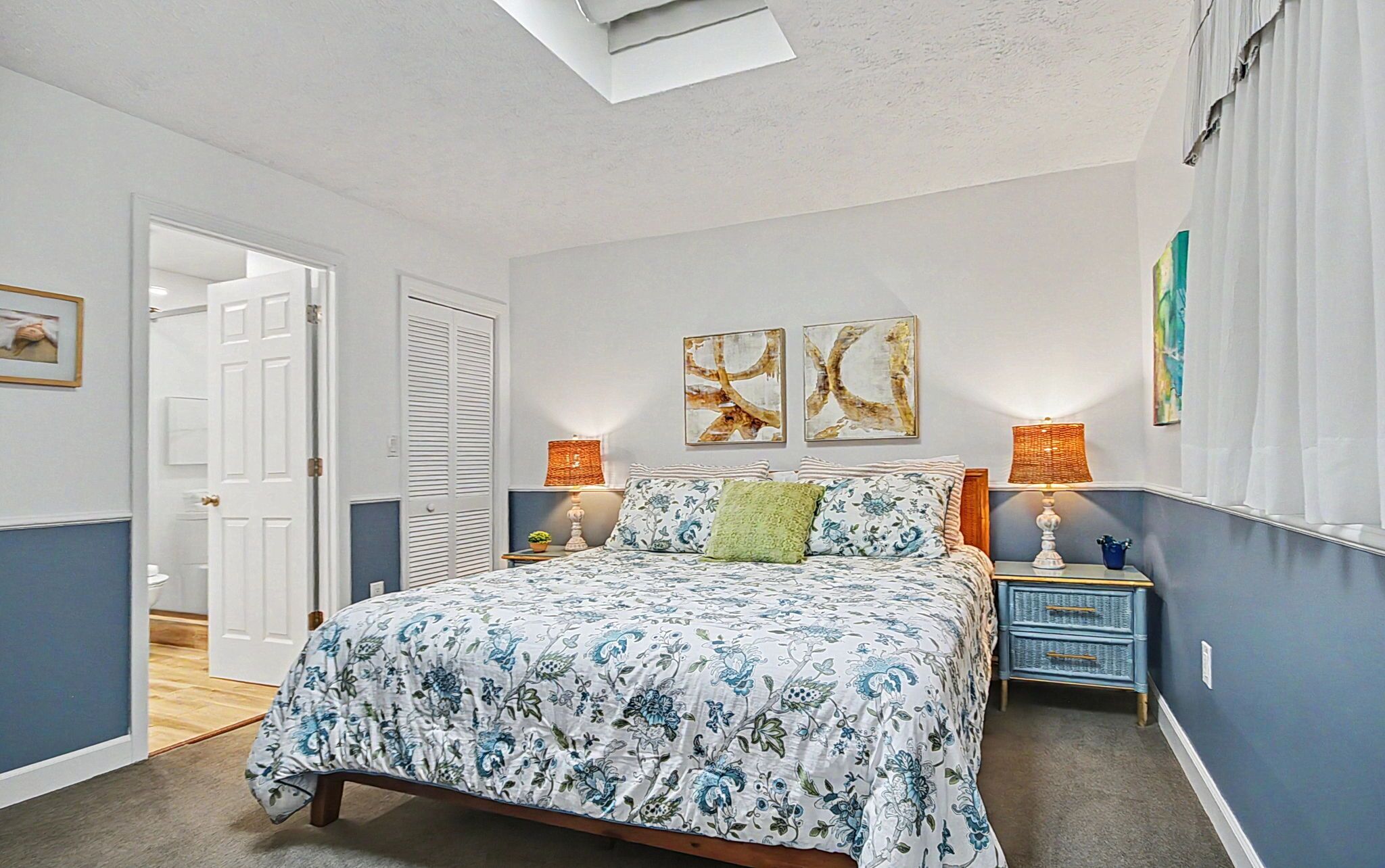 A bedroom with a bed, two wall-mounted lamps, a nightstand, a door, and a window with curtains.