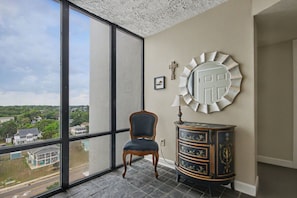Une pièce dotée d’une grande fenêtre, d’un fauteuil, d’un meuble décoratif et d’un miroir fixé au mur.