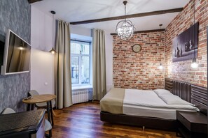 Relax in a cozy space with a large bed, round table, and chair, surrounded by exposed beams and a rustic brick accent wall.