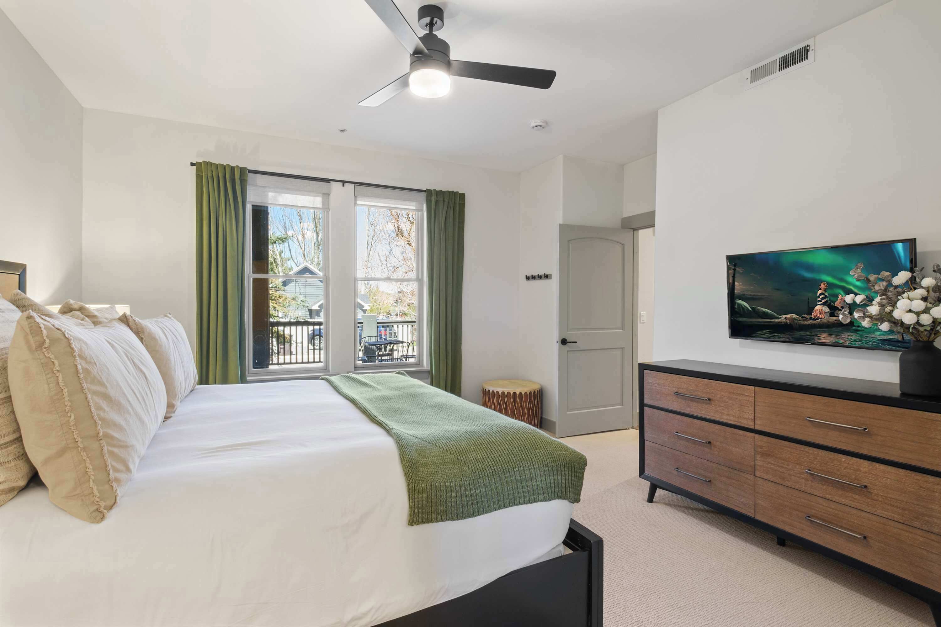 A bedroom with a bed, a TV, a dresser, and a window with curtains.