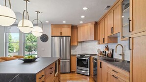 A modern kitchen with wooden cabinets, stainless steel appliances, and pendant lighting. - The Moose Lodge - New 2BR, Walk to PCMR / Main St! (Park City)