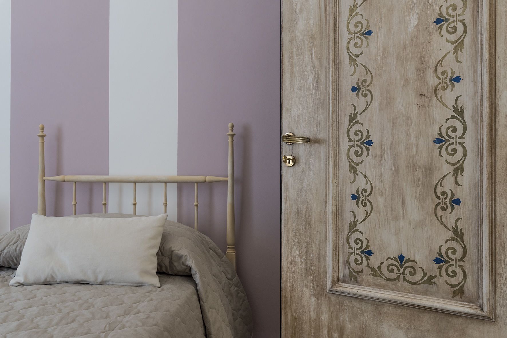 A bed with a headboard, a door with decorative paneling, and a wall with vertical stripes.