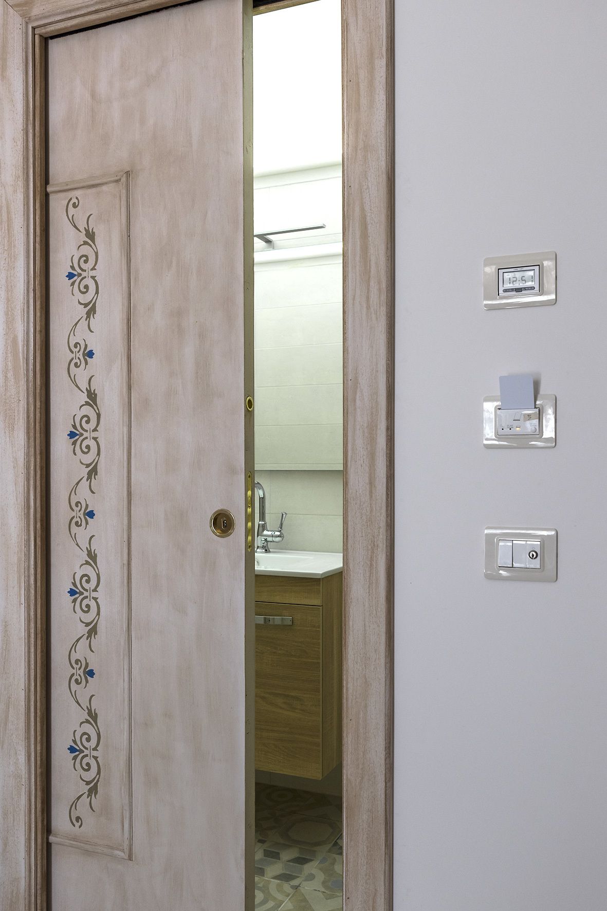 Een deur met een decoratief paneel en een uitzicht op een badkamer met een wastafel en kastjes.