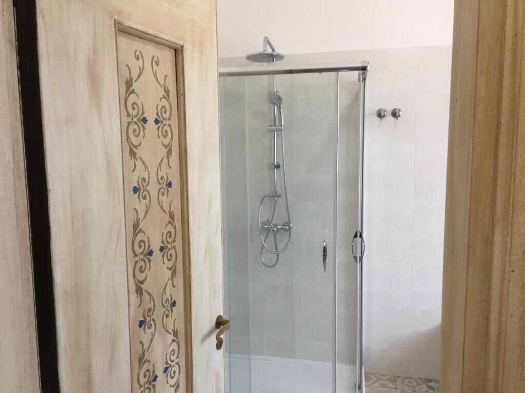 Une douche fermée par des parois en verre, dotée d’un pommeau de douche à main et d’un robinet fixé au mur.
