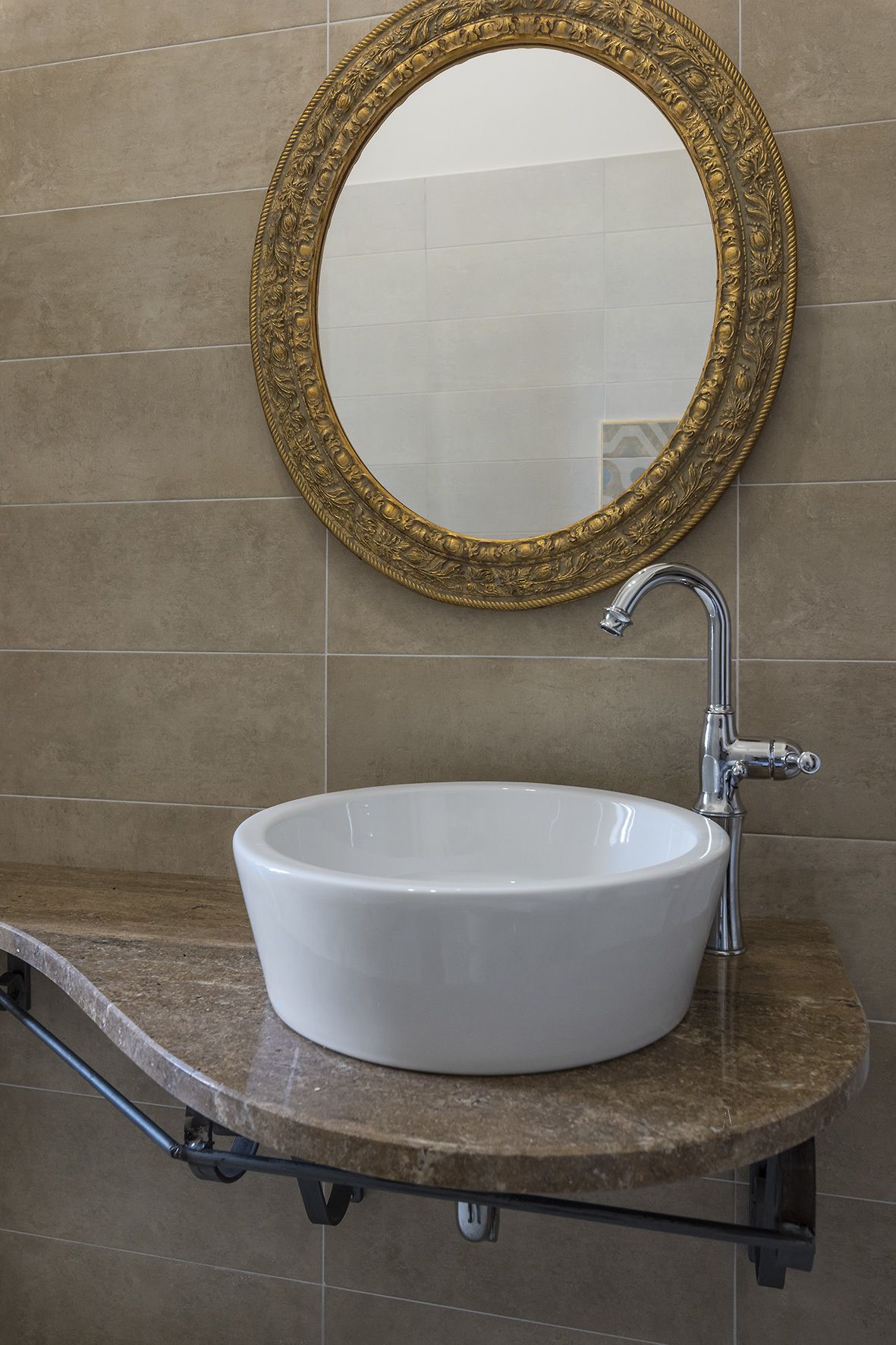 Un baño con un lavamanos blanco, un espejo con marco dorado y un grifo moderno.