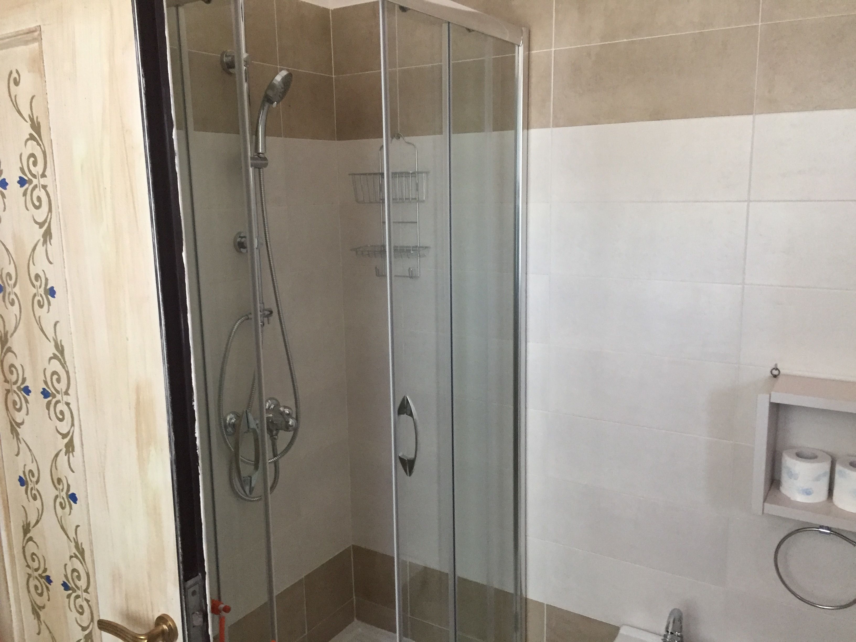 Zona de ducha con mampara de vidrio, cabezal de ducha y ducha de mano.