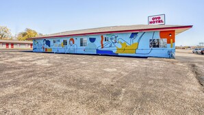 Un motel con un mural en la pared, un cartel que dice 'OYO HOTEL' y un estacionamiento al frente.
