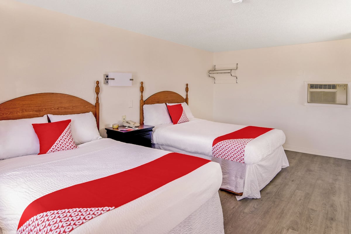 A hotel room with two beds, each with a wooden headboard, white bedding, and red accents. There is a nightstand with a lamp and a telephone.
