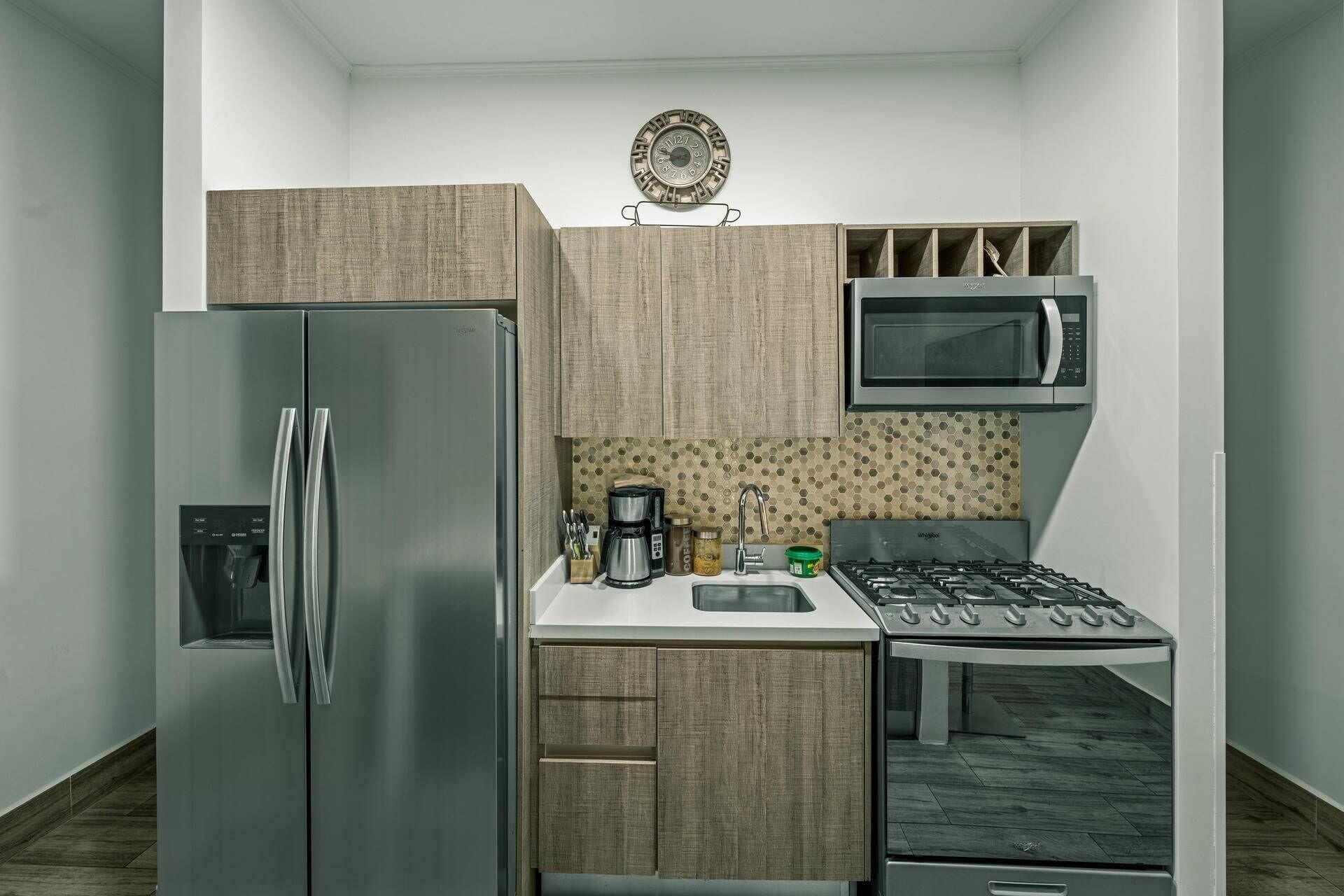 A compact kitchen with a stainless steel refrigerator, a microwave, a coffee maker, and a gas stove.