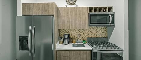 A compact kitchen with a stainless steel refrigerator, a microwave, a coffee maker, and a gas stove.