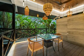 Une terrasse en bois avec une table en verre et des chaises en osier, entourée d’une végétation luxuriante et agrémentée d’une balustrade en bois.