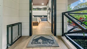 Ein Hotelkorridor mit Holzboden, einem Bett im Hintergrund und einem Balkon mit Pflanzen.