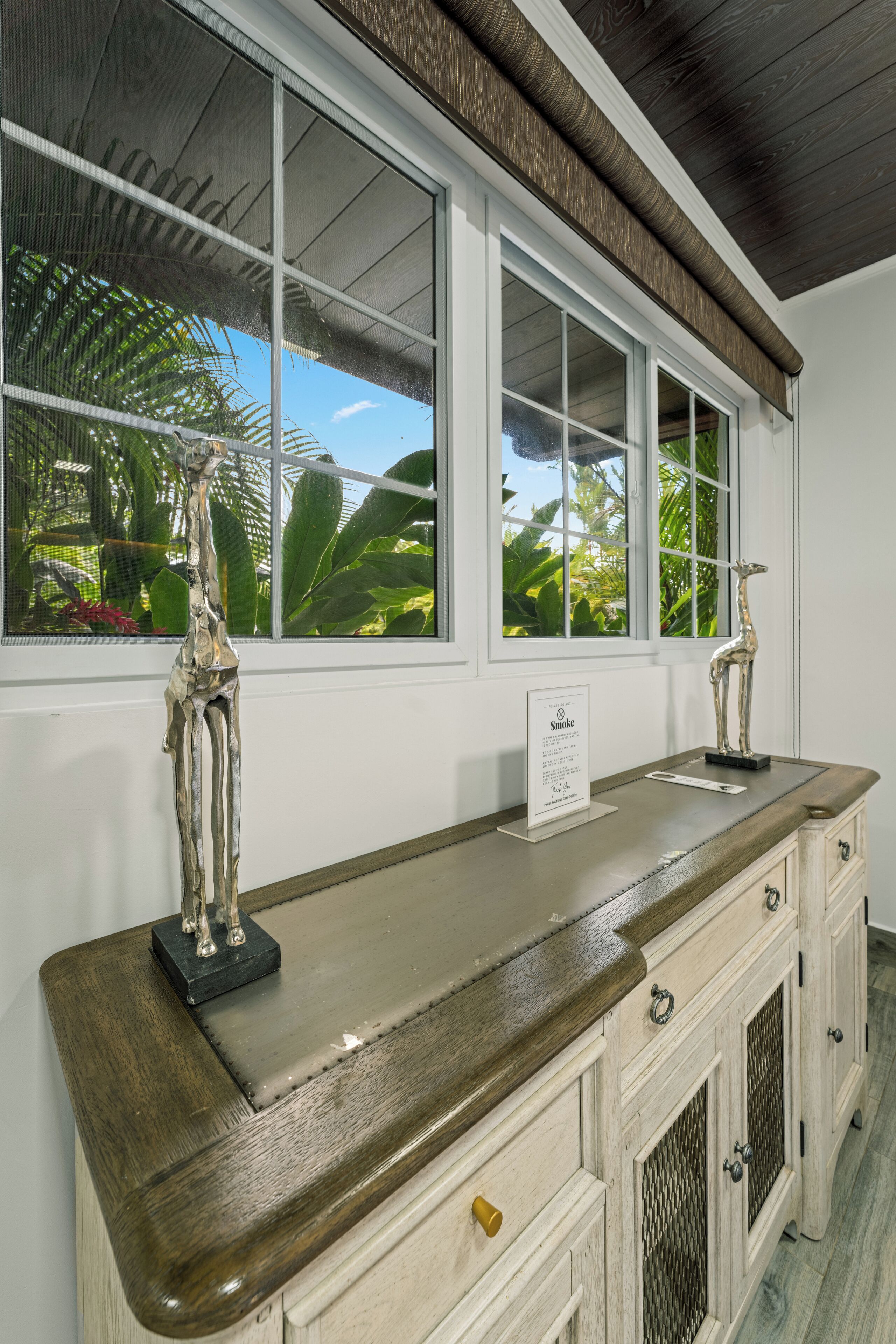 Una encimera de madera con dos estatuas de plata, una ventana con vistas a follaje, y un certificado enmarcado sobre la encimera.