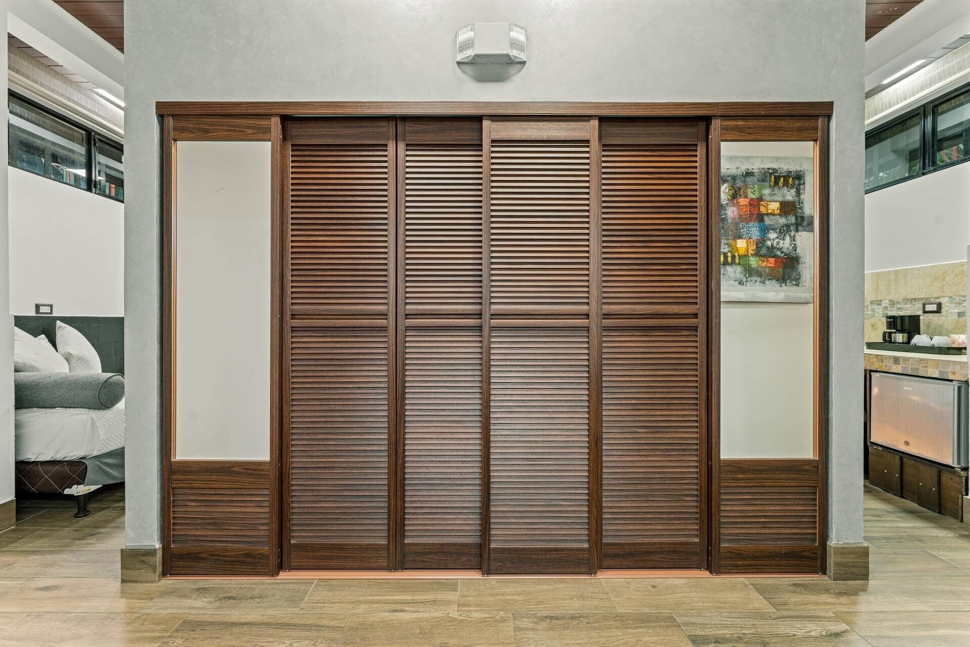 A room with a large wooden sliding door, a bed with white bedding, and a kitchen area with a countertop and appliances.