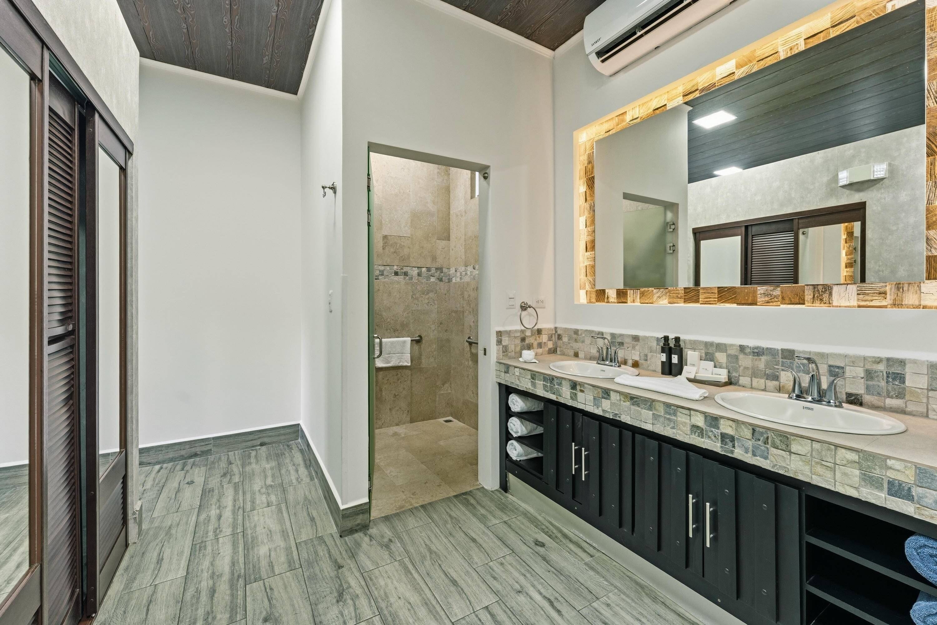 A modern bathroom with a large mirror, two sinks, and a shower area.