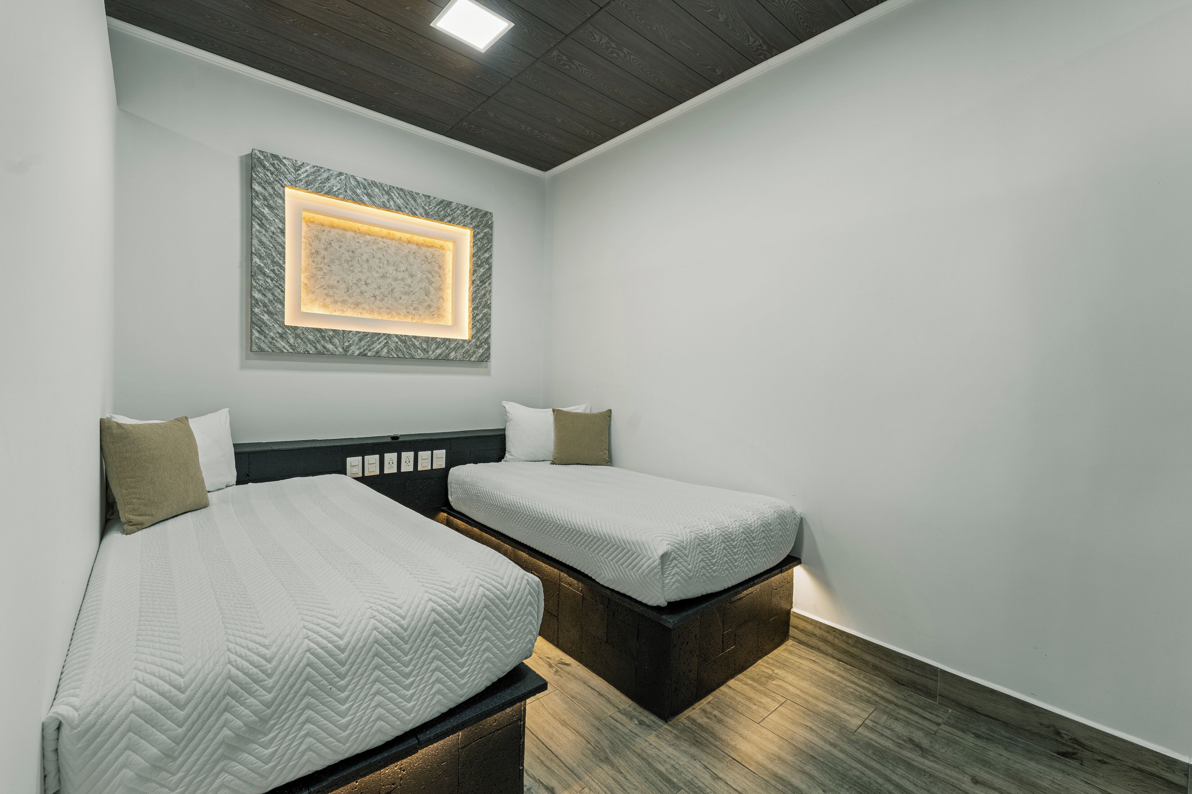 A hotel room with two beds, a framed artwork on the wall, and a wooden ceiling.