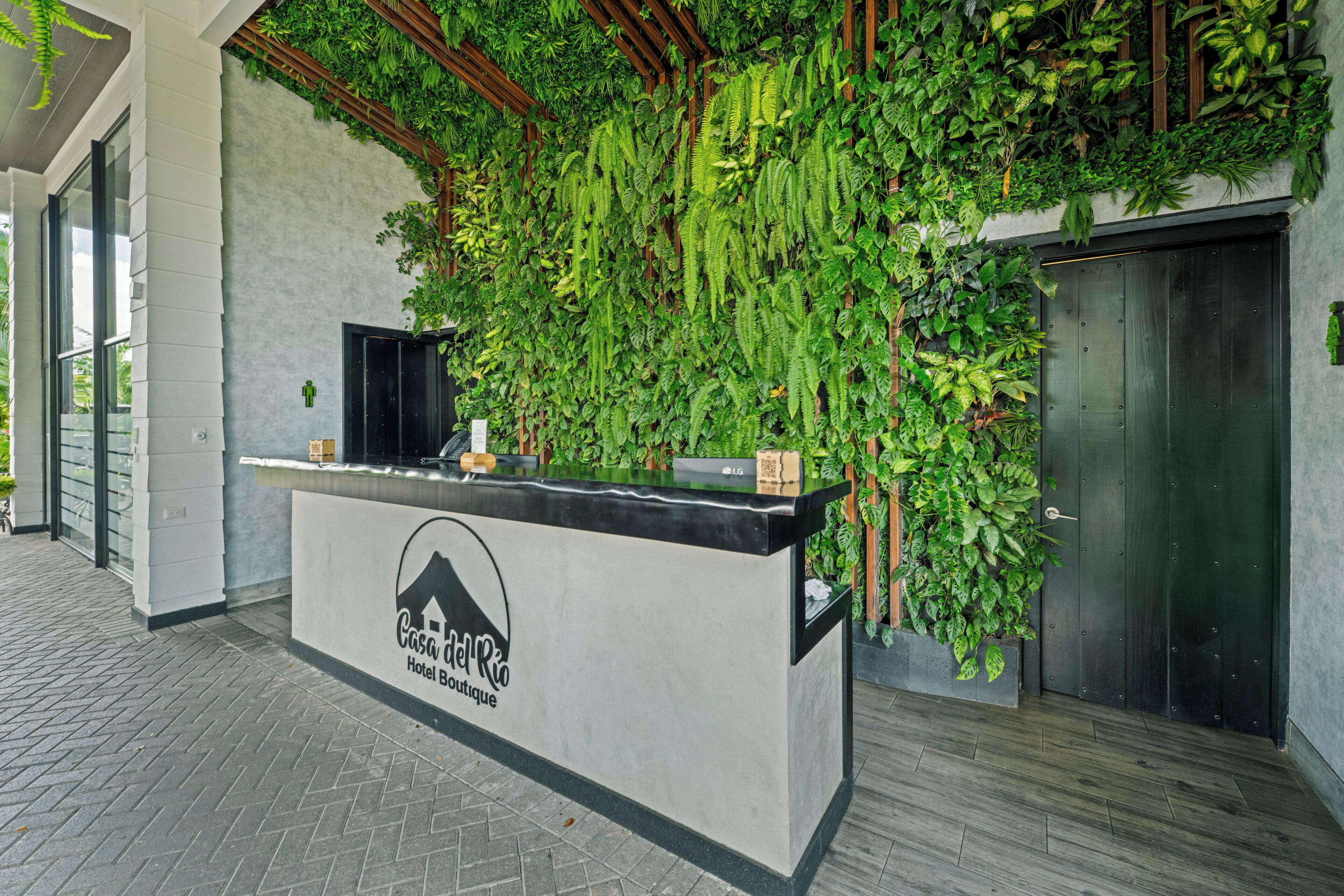 Una reception con il logo dell'Hotel Boutique Casa del Rio, circondata da piante verdi rigogliose e un design moderno.
