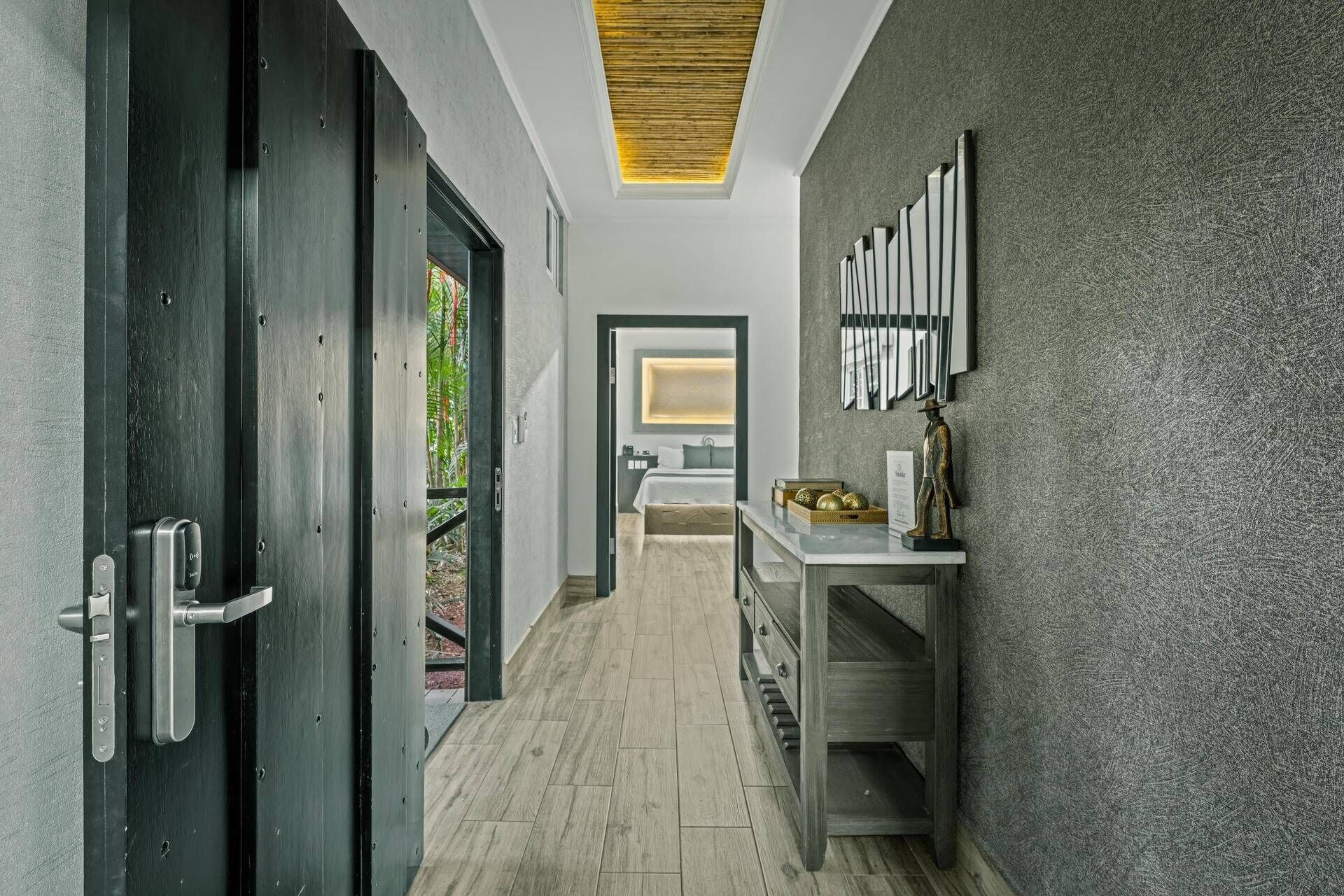 A hallway with a wooden floor, a dark door, and a wall-mounted shelf with decorative items.