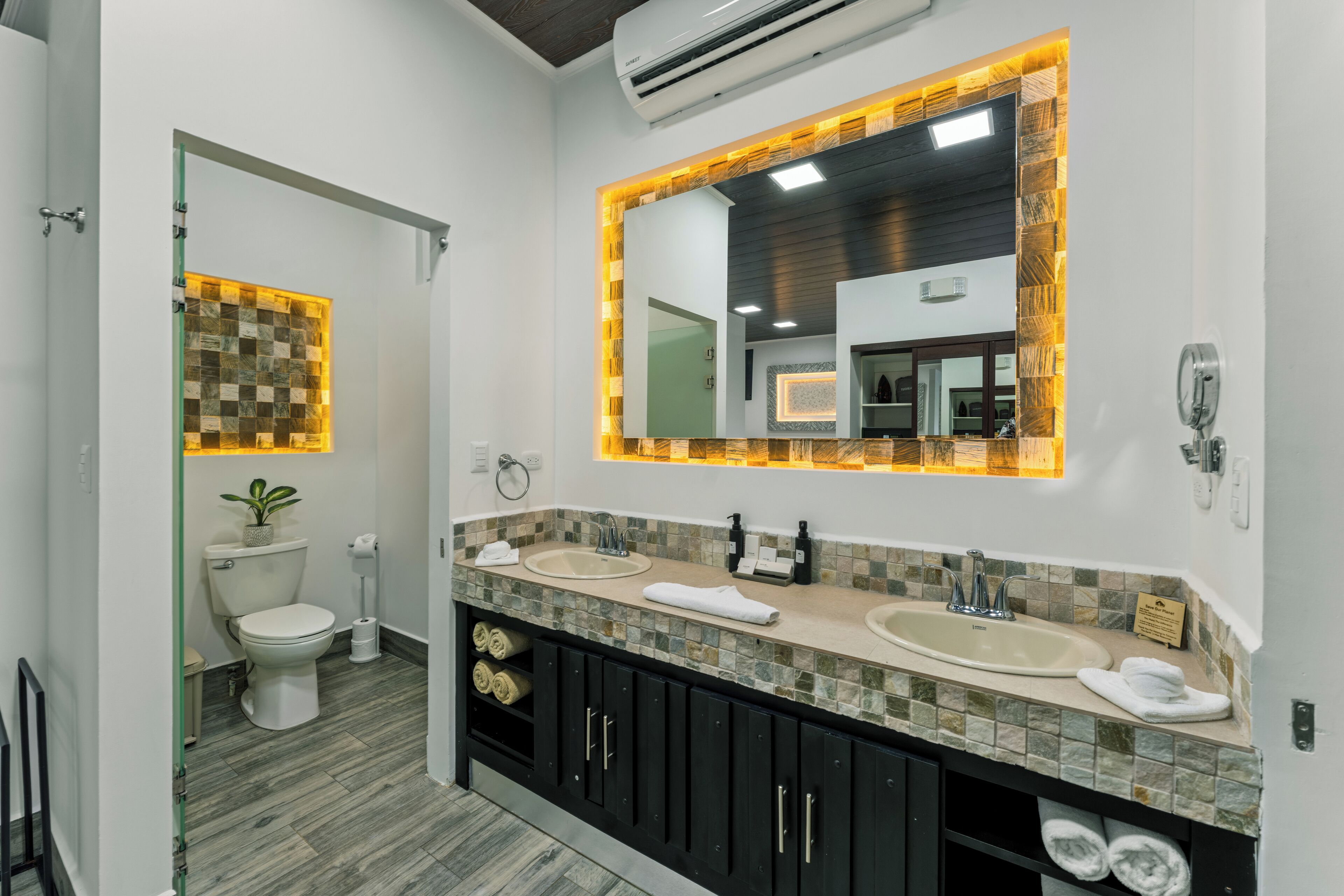 A modern bathroom with two sinks, a large mirror, and a toilet.