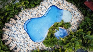 Vue aérienne d’une piscine entourée de palmiers et de chaises longues.