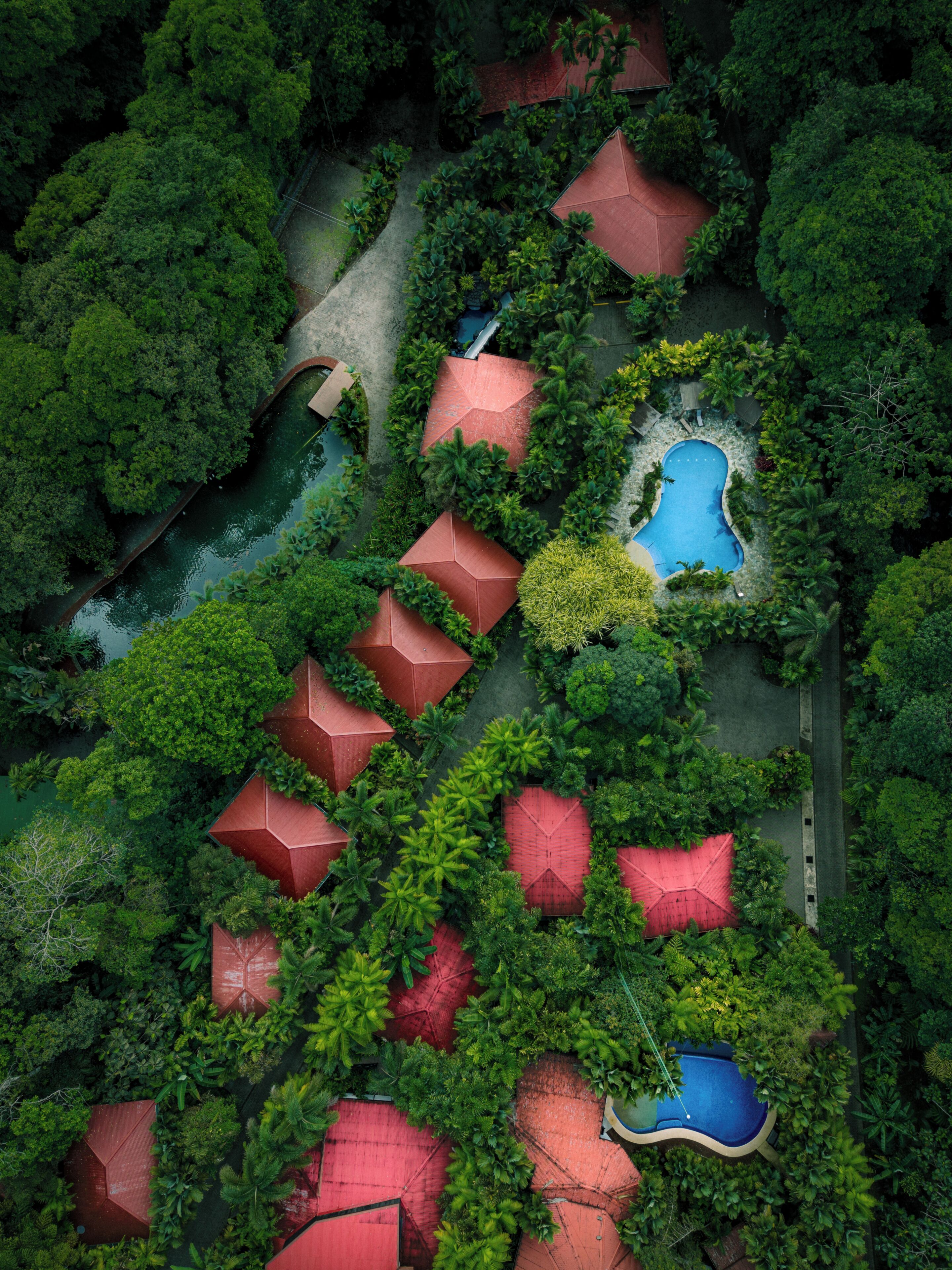 Vista aérea de un complejo turístico con varias edificaciones de techo rojo, una piscina central y abundante vegetación circundante.