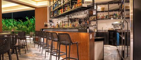 Zona de bar con mostrador de madera, varias estanterías con botellas y taburetes.
