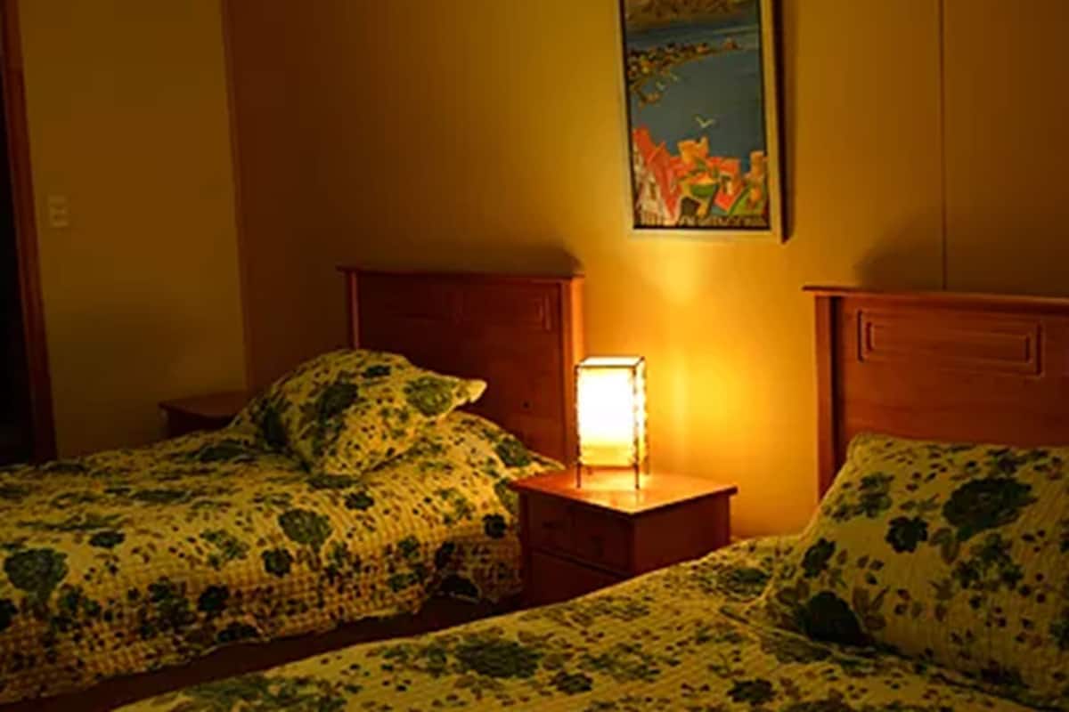 A room with two beds, each with a patterned blanket, a bedside table with a lamp, and a framed picture on the wall.