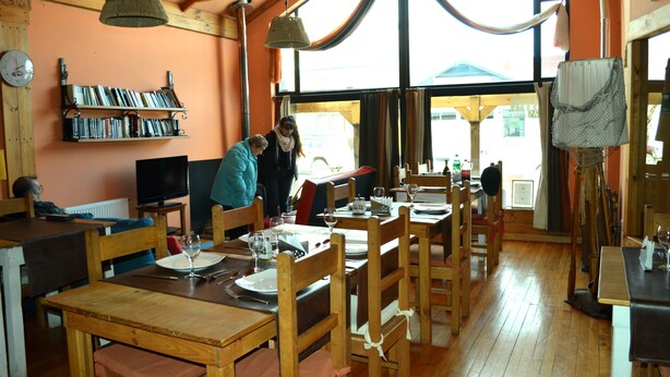 Ein gemütliches Restaurant mit Holzkuben, einem Bücherregal voller Bücher und großen Fenstern.