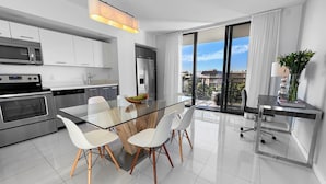 A modern kitchen with stainless steel appliances, a glass dining table, and a view of the city through large windows. - Bay Breeze Premium Apartments By Eskape Collection (Bay Harbor Islands)