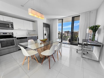 A modern living room with a glass dining table, yellow chairs, and a large mirror. at Bay Breeze Premium Apartments By Eskape Collection