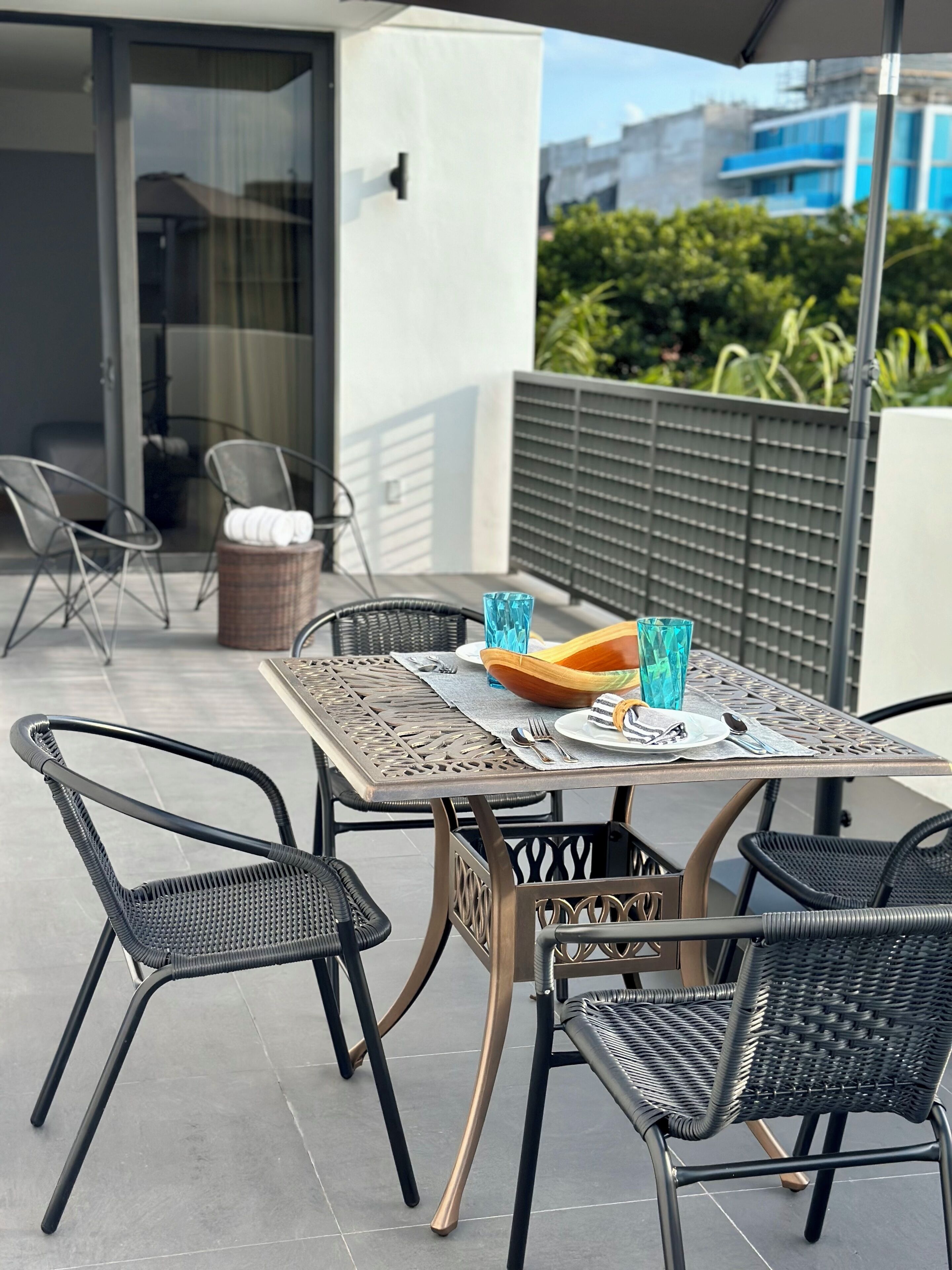 An outdoor patio with a table set for dining, surrounded by wicker chairs.