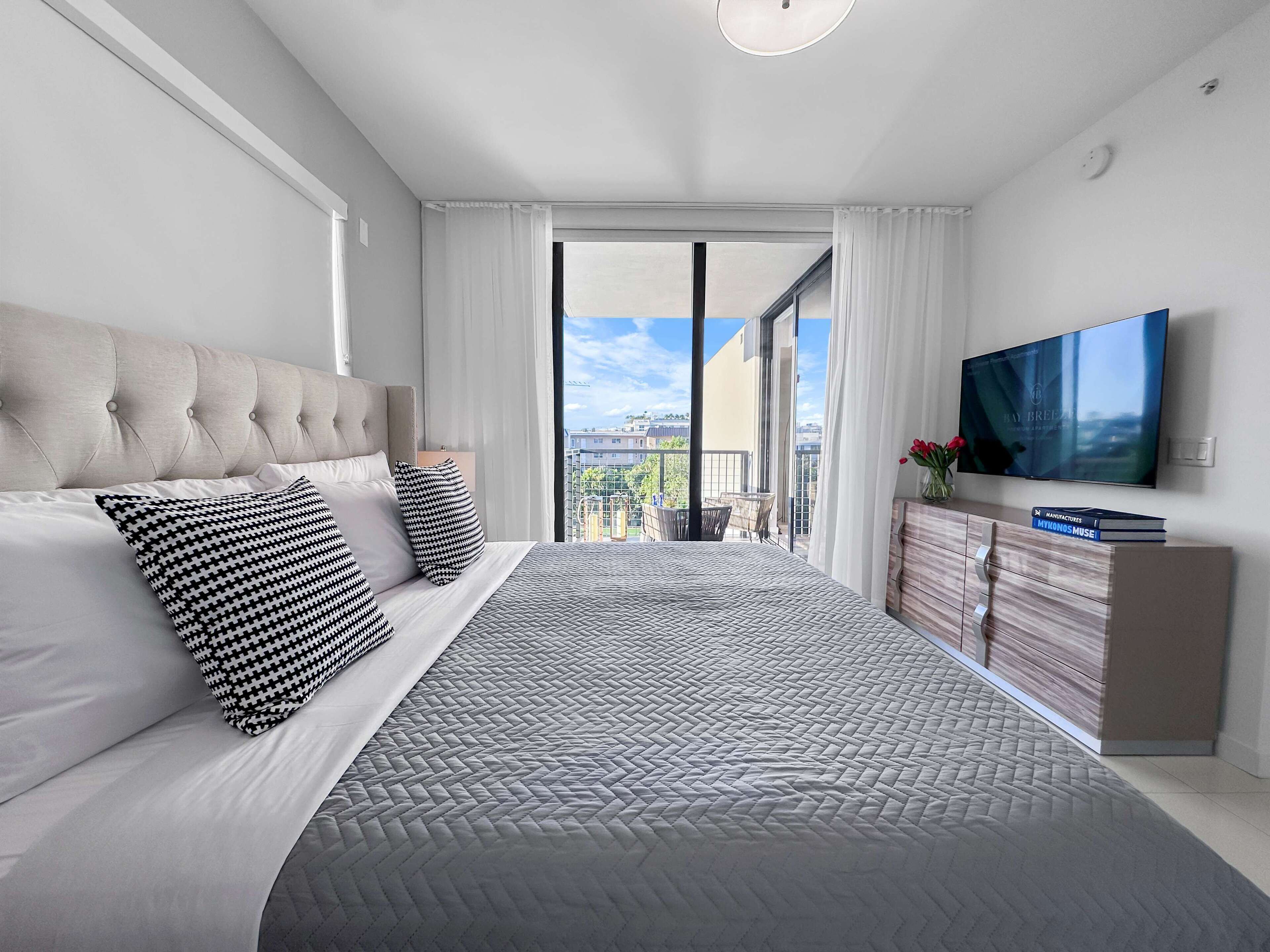 A modern bedroom with a large bed, a TV, and a view of the city.