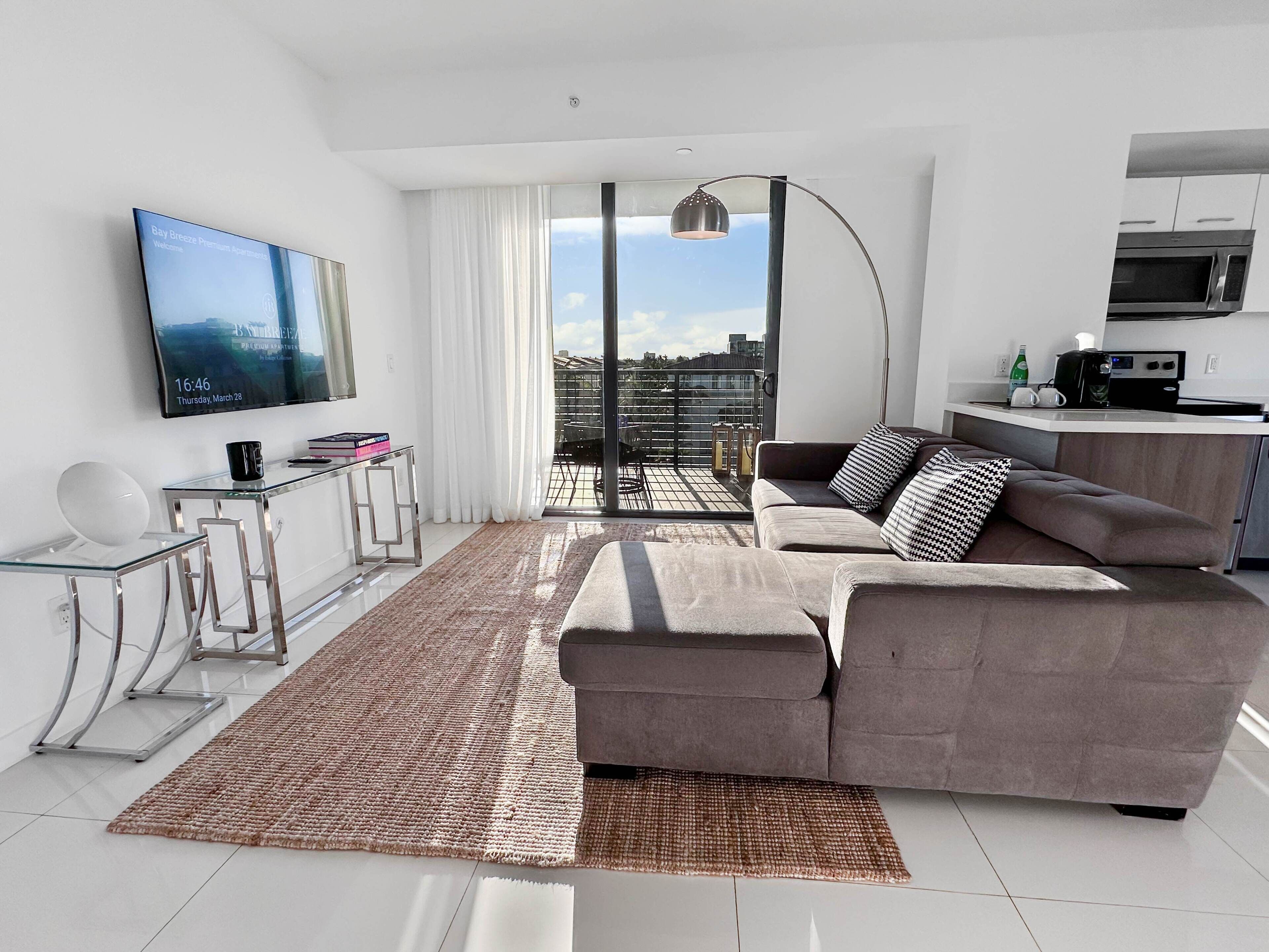 Una sala de estar moderna con un sofá gris, una mesa de centro de vidrio y un televisor de pantalla plana montado en la pared.