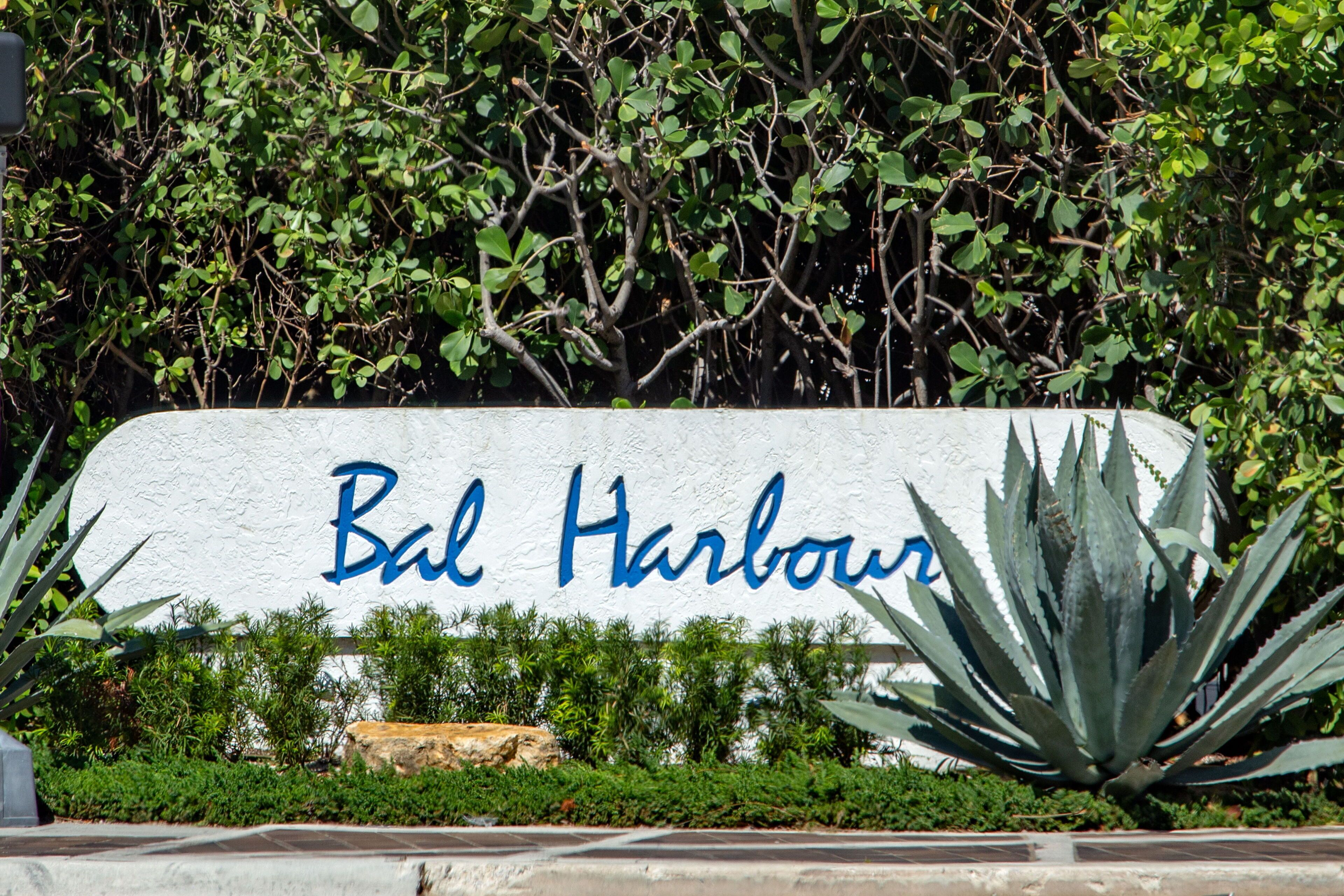A sign with 'Bal Harbour' written on it, surrounded by greenery and a large agave plant.