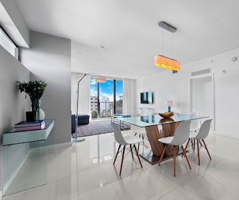 A modern, well-lit living room with a large window, a dining area with a glass table, and a sofa. at Bay Breeze Premium Apartments By Eskape Collection