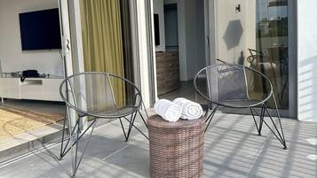 Un balcon moderne avec deux chaises en métal, un panier en osier contenant des serviettes et un téléviseur fixé au mur.