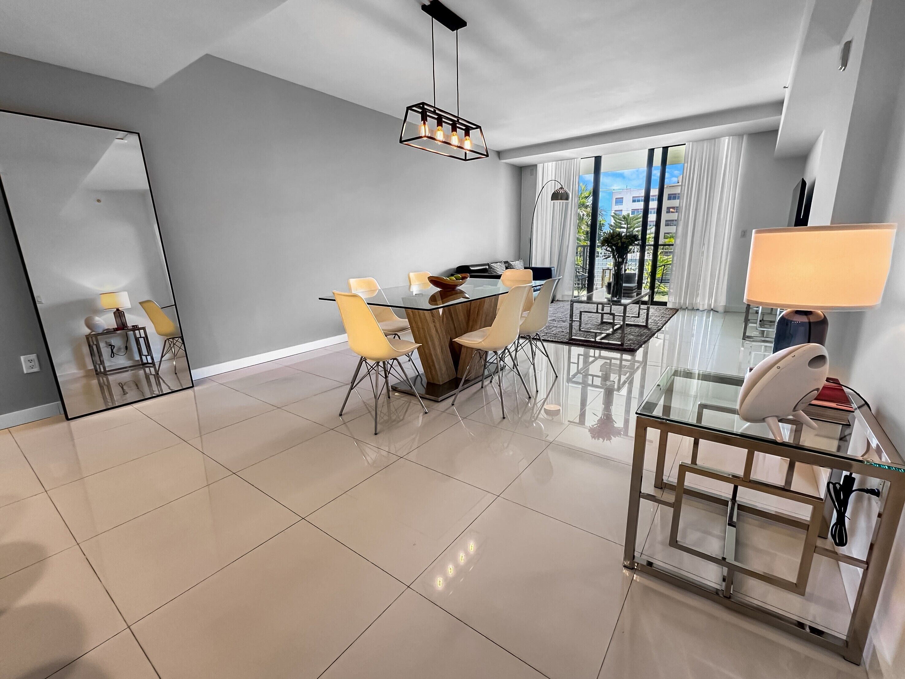 A modern living room with a glass dining table, yellow chairs, and a large mirror.