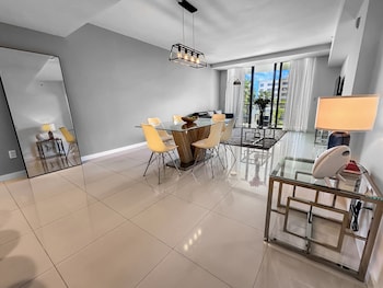 A modern dining area with a glass table, white chairs, and a vase of flowers. at Bay Breeze Premium Apartments By Eskape Collection
