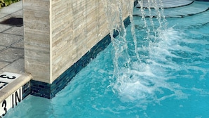 A pool with a waterfall feature, a 3-inch depth marker, and a metal handrail. - Bay Breeze Premium Apartments By Eskape Collection (Bay Harbor Islands)