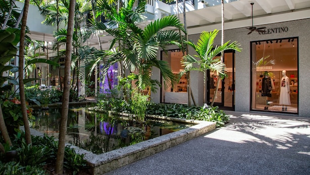 A shopping mall with a central water feature, surrounded by lush greenery and palm trees. - Bay Breeze Premium Apartments By Eskape Collection (Bay Harbor Islands)