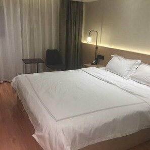 A hotel room with a large bed, a desk, a chair, and a nightstand with a lamp. - Xingwei Hostel (Wuhan)