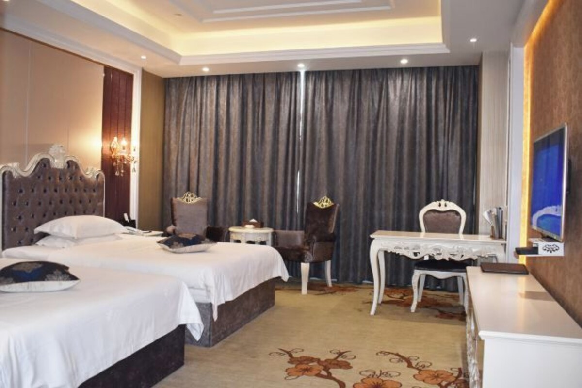 A hotel room with two beds, a desk, a chair, a television, and a curtain.