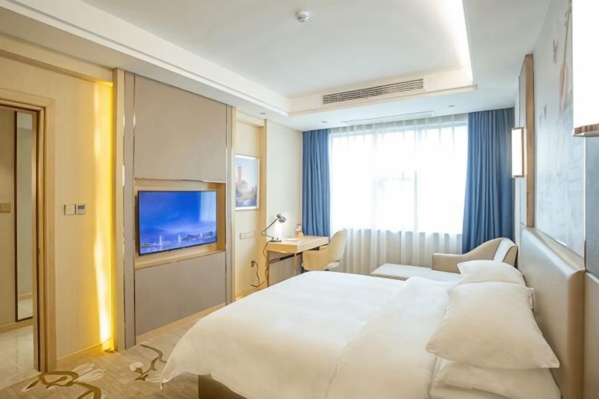 Una camera d'albergo con un letto, una scrivania, televisione e ampie finestre.