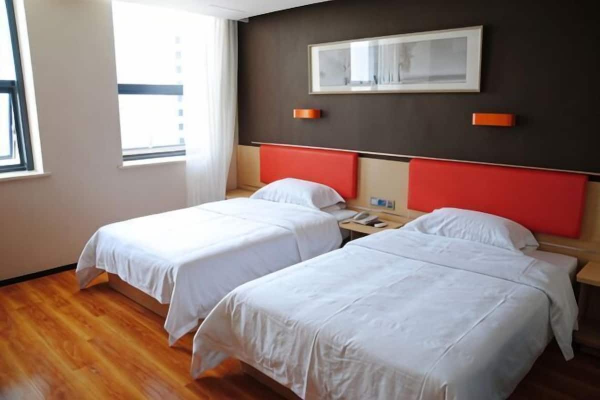 Habitación de hotel con dos camas, una ventana, un teléfono de pared y un cuadro enmarcado.