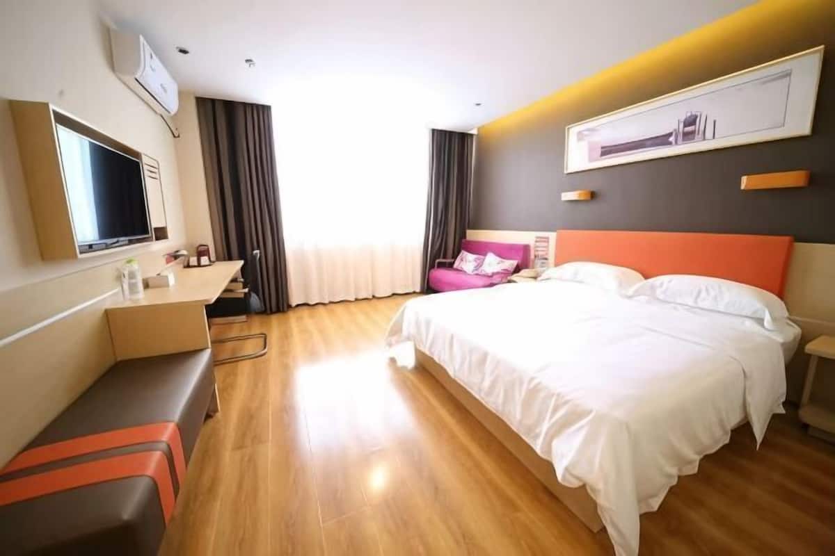 Una habitación de hotel con cama, escritorio, silla, televisor y ventana con cortinas.
